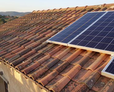 Toiture ancienne en tuiles de terre cuite inspectée à côté de panneaux solaires récemment installés.